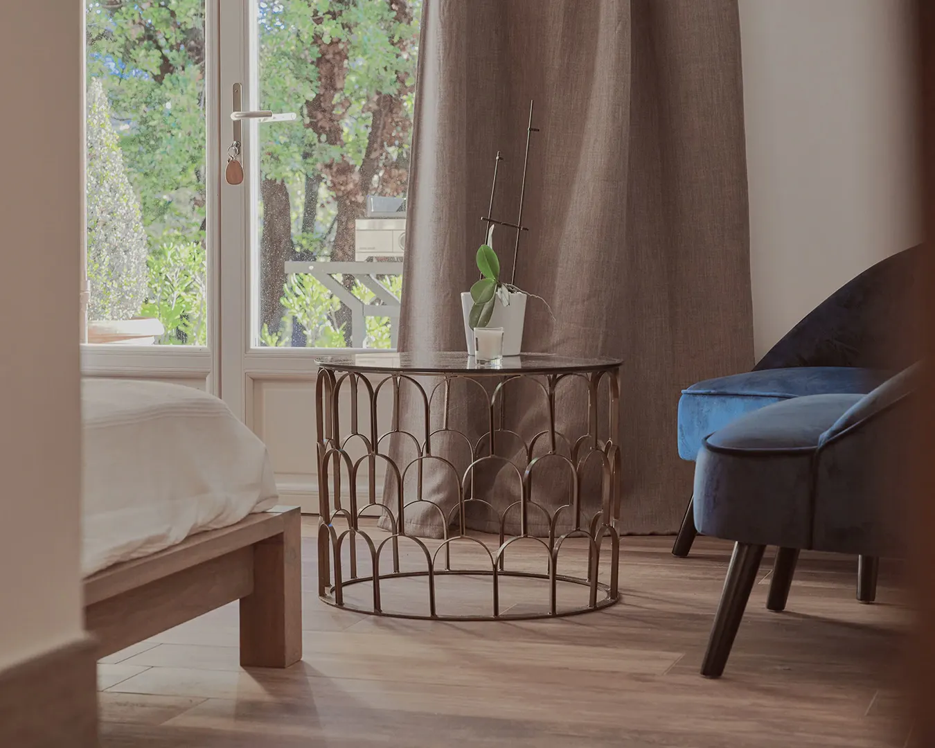 Coin chambre lumineux : guéridon design, fauteuil bleu et lit près d'une baie vitrée, photographie d'intérieur immobilier