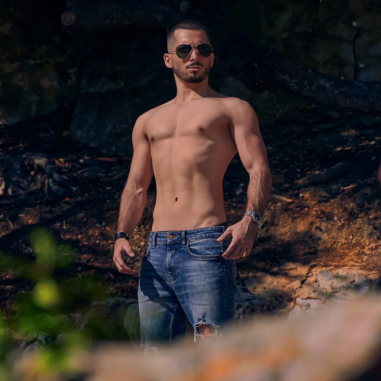 Athlète torse nu en jean et lunettes aviateur, musculature sculptée par la lumière en sous-bois, photographe fitness Suisse romande & France