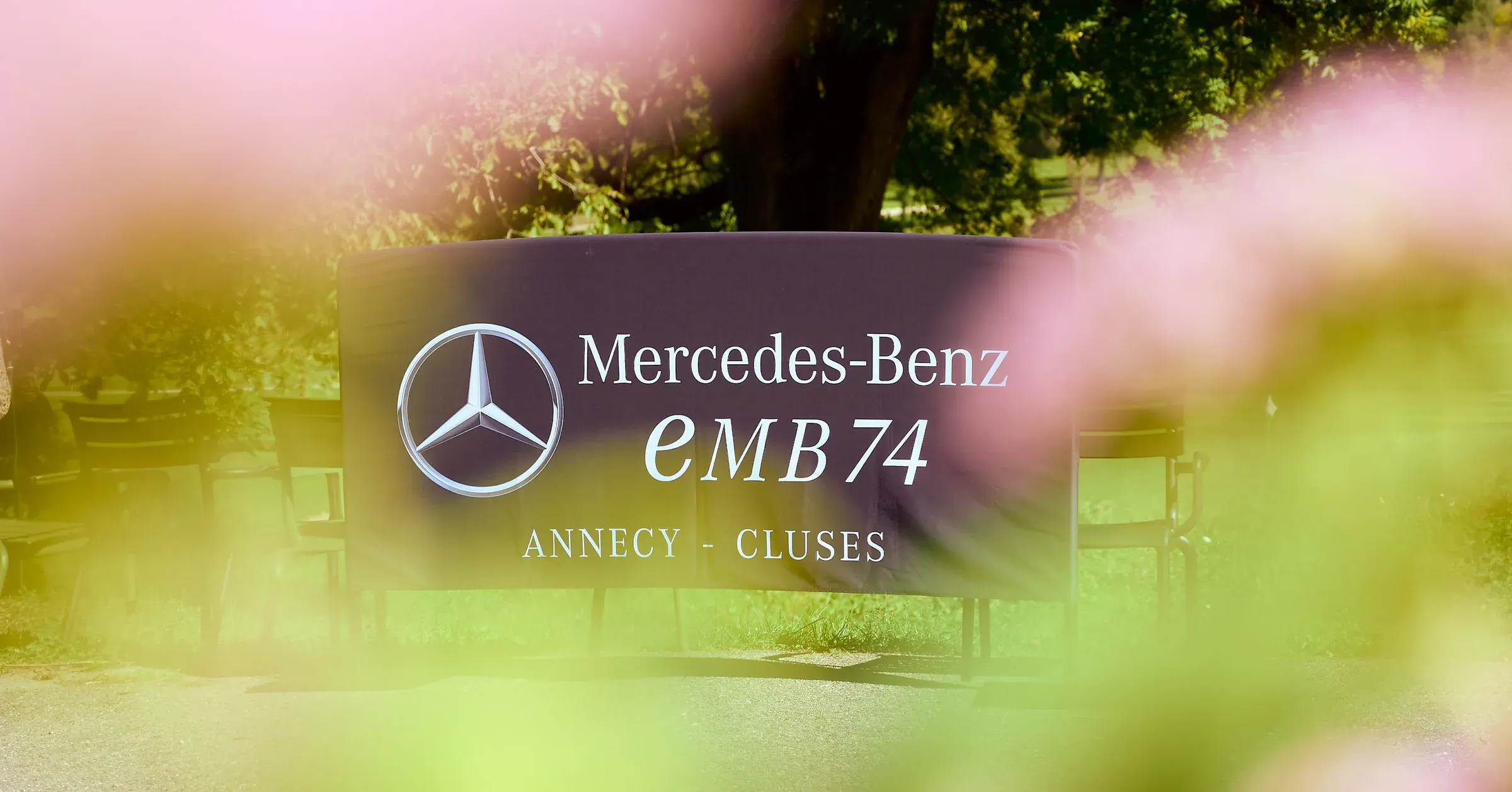 Bannière Mercedes-Benz EMB à travers un premier plan fleuri flou, photographie événementielle automobile au golf de Giez