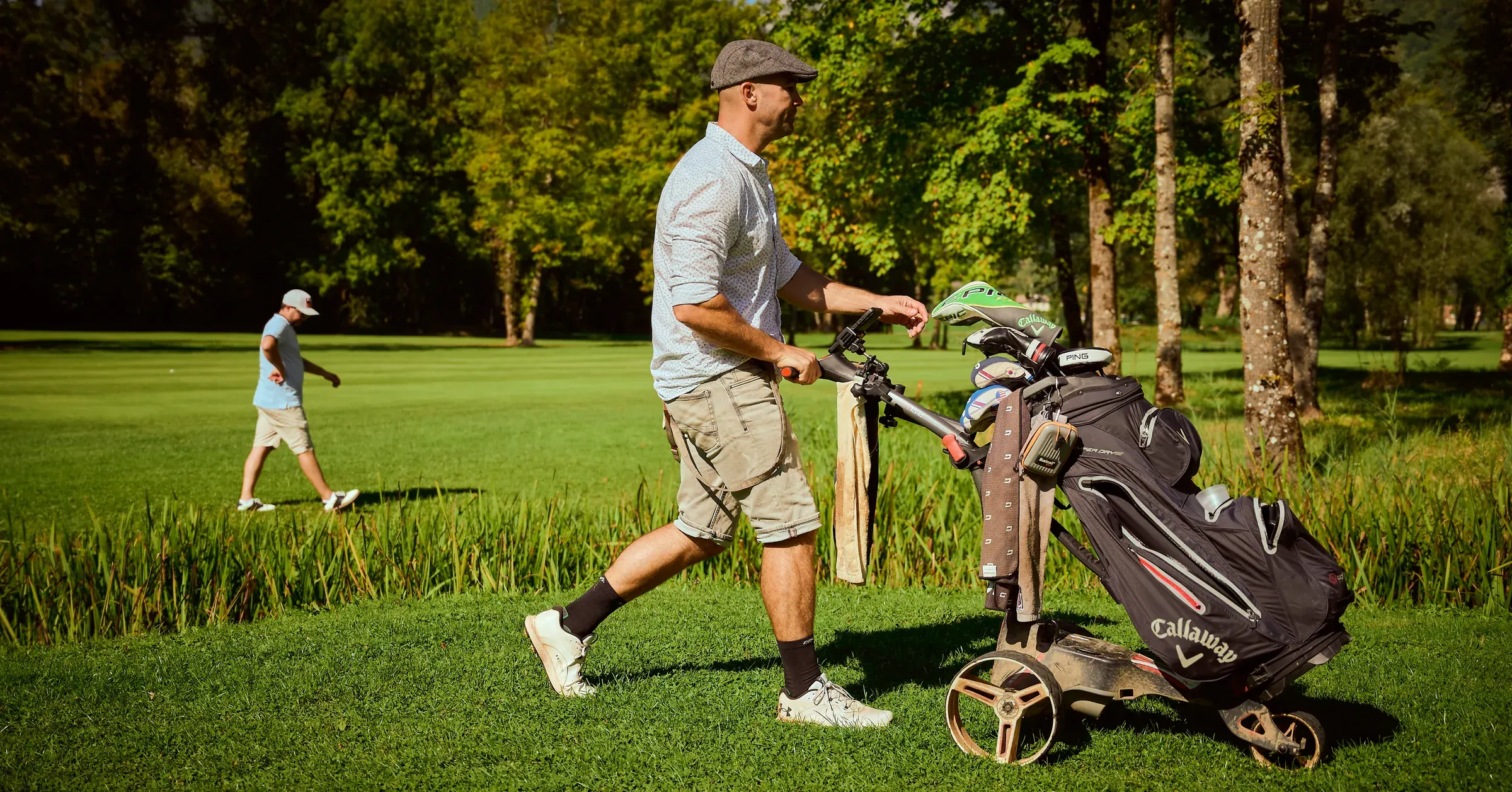 Golfeur en casquette plate poussant son chariot Callaway sur le parcours ensoleillé de Giez, reportage du photographe