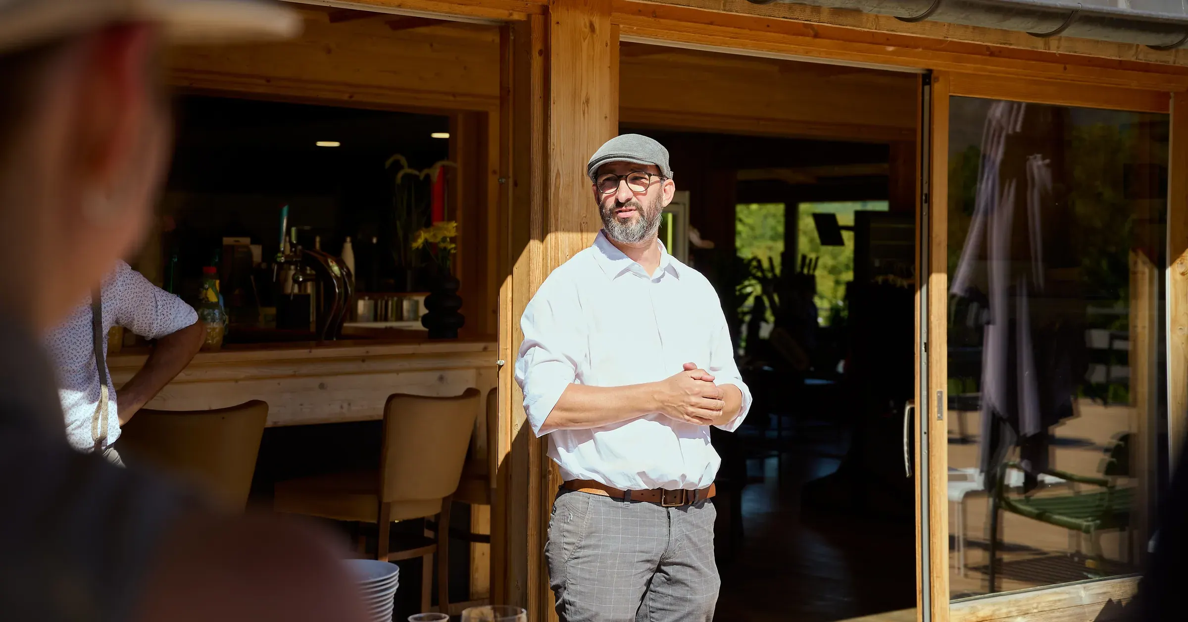 Orateur en chemise blanche et casquette au soleil devant le club-house en bois, reportage événementiel automobile à Giez