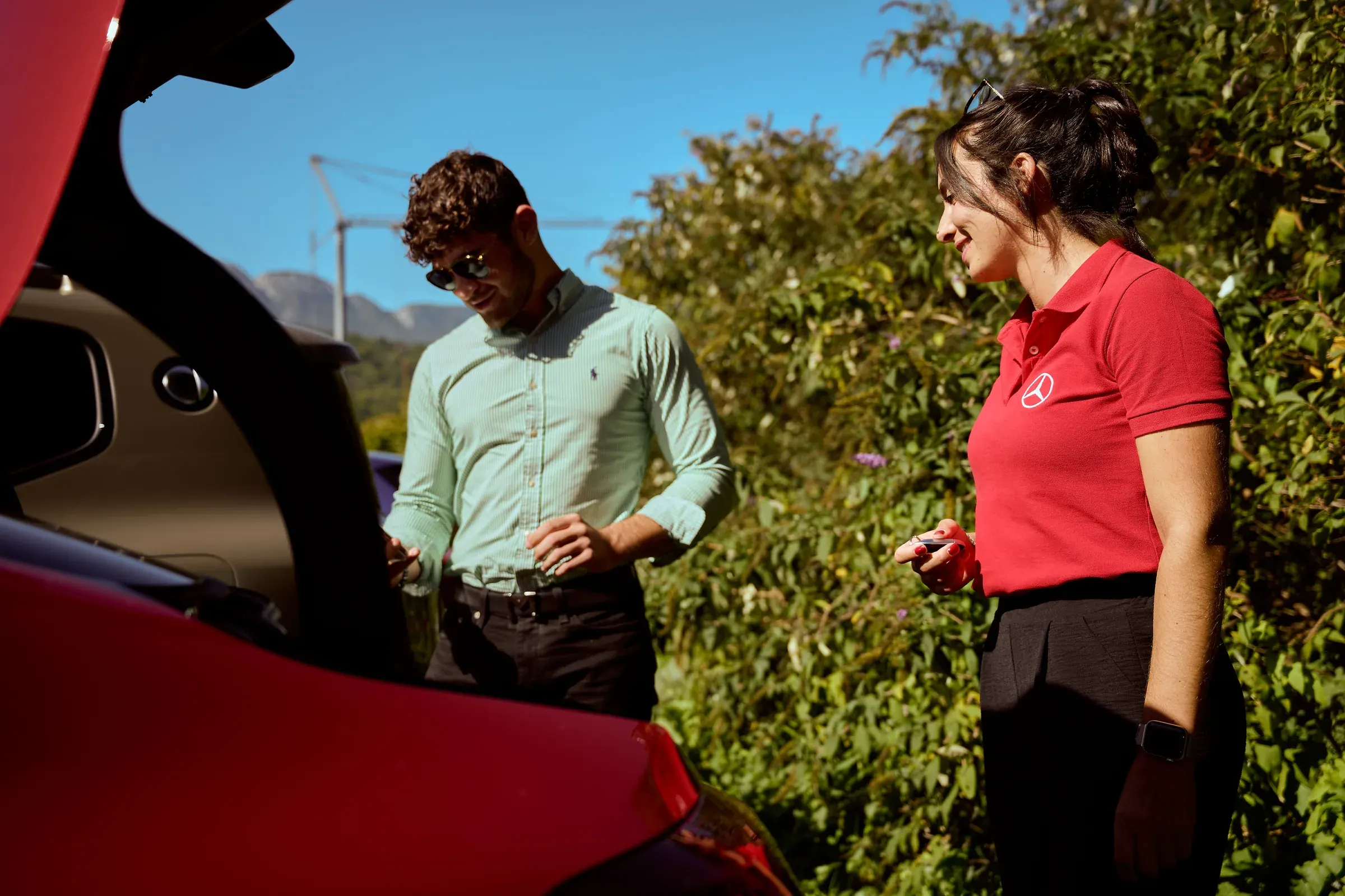 Hôtesse Mercedes-Benz tenant une clé près d’un invité qui découvre le coffre d’une voiture rouge à Giez, reportage automobile