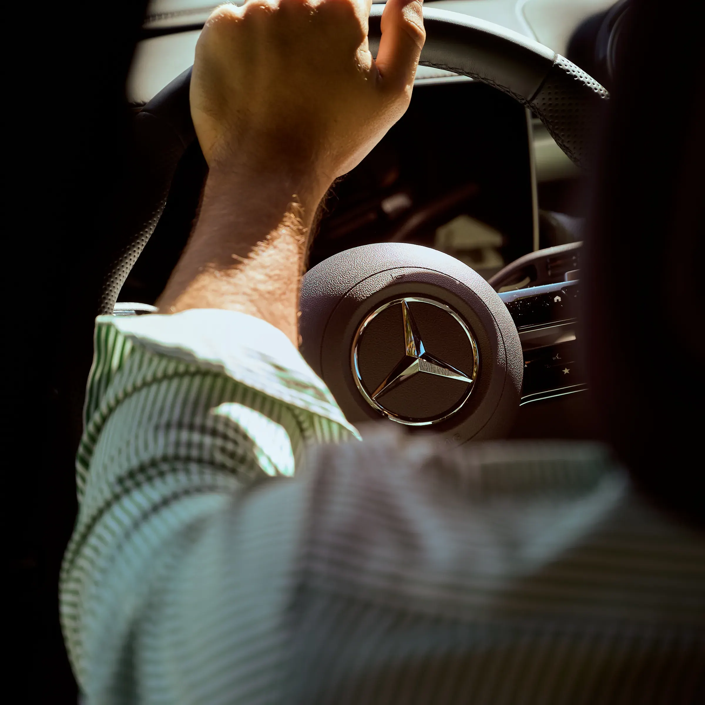 Main d'un conducteur sur le volant cuir d'une Mercedes-Benz, étoile chromée en lumière, photographie automobile à Giez