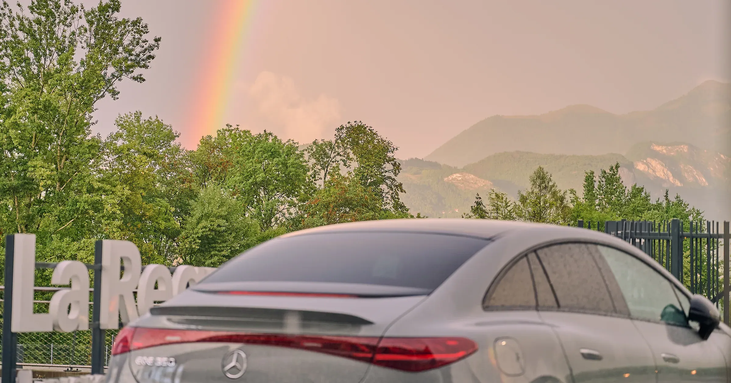 Mercedes-Benz EQE grise perlée de pluie sous un arc-en-ciel face aux Préalpes, La Roche-sur-Foron, photographe automobile