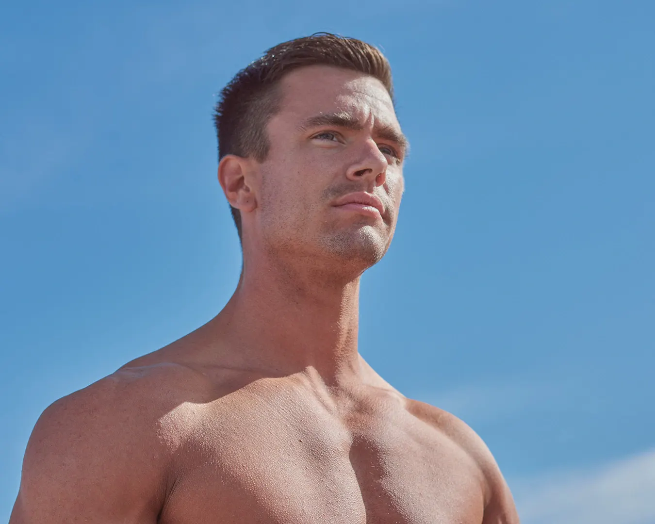 Athlète masculin torse nu au regard déterminé sous un ciel bleu, portrait fitness par photographe à Nice