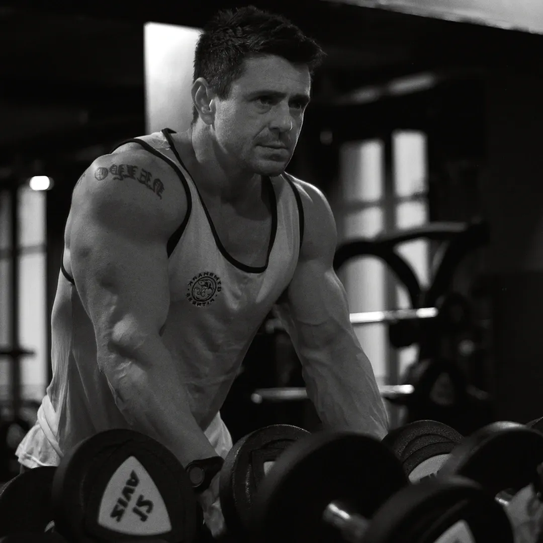 Athlète musclé en débardeur soulevant des haltères dans une salle de sport, portrait fitness en noir et blanc