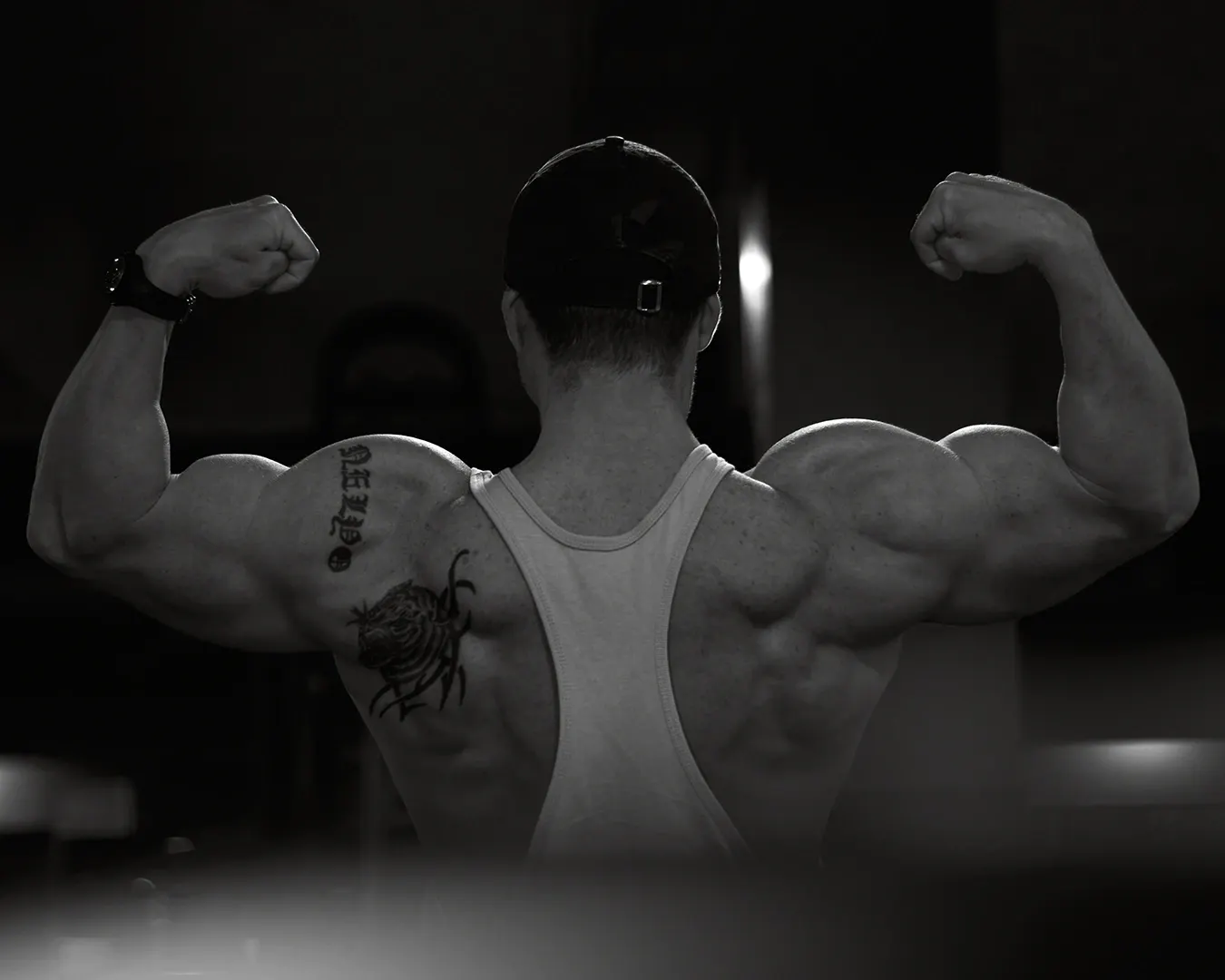 Bodybuilder de dos en double biceps, dos musclé et tatouage, séance photo fitness en salle, noir et blanc