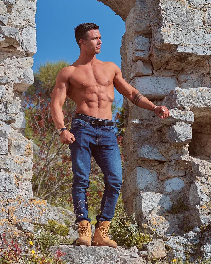 Athlète torse nu musclé en jean posant dans des ruines de pierre, séance photo fitness en extérieur sur la Côte d'Azur