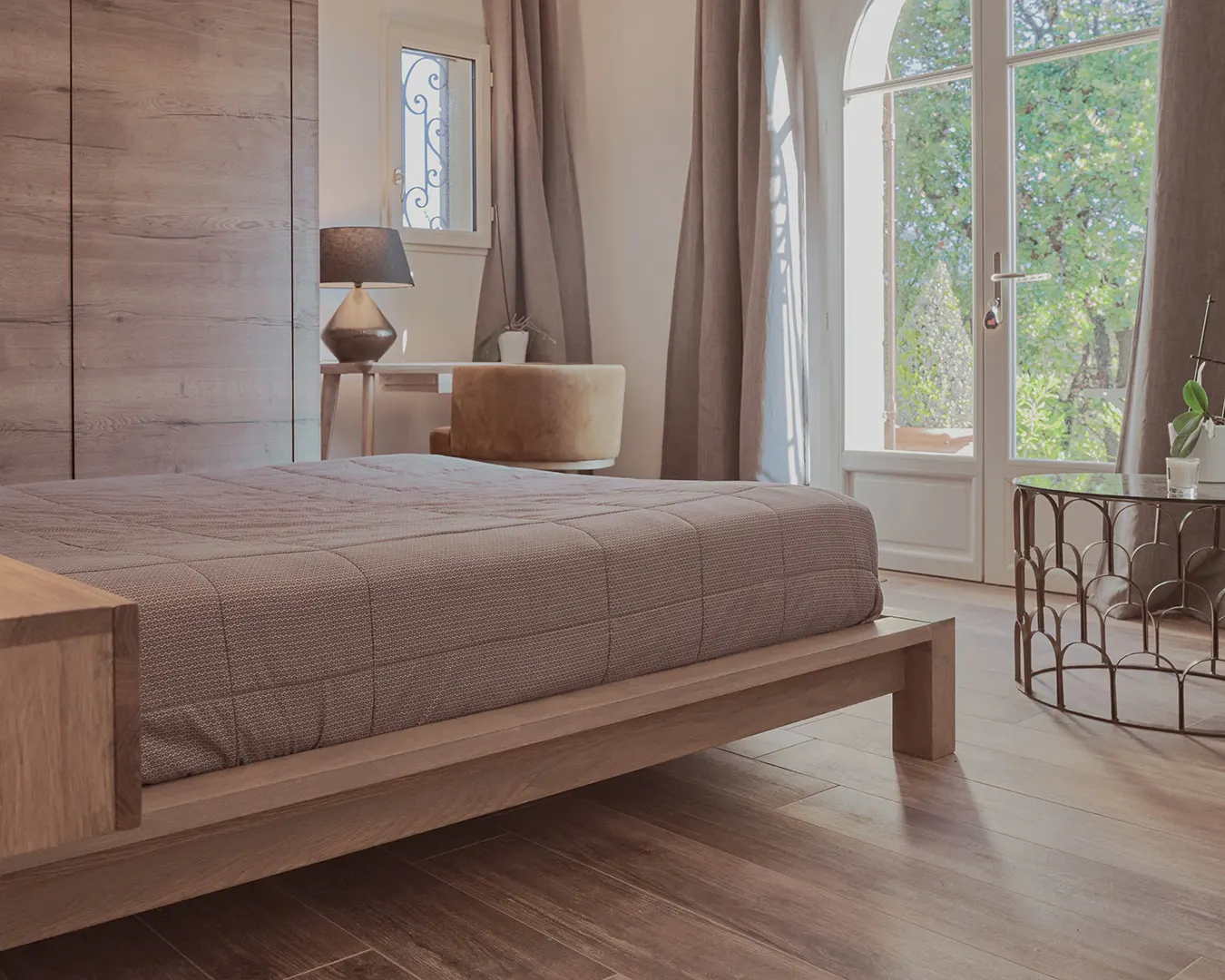 Chambre principale aux tons bois et lin, baie vitrée ouverte sur jardin, photographie immobilière haut de gamme en Suisse romande