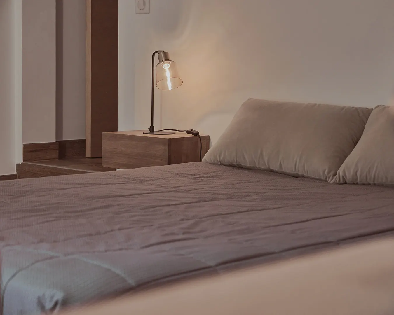 Chambre épurée aux tons beige, lit double et lampe de chevet allumée, photographie immobilière d'intérieur haut de gamme
