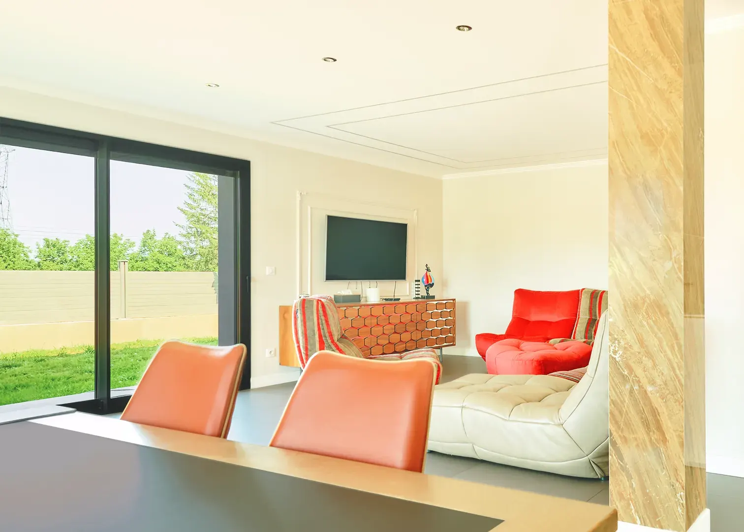 Salon design d'une villa contemporaine, baie vitrée sur jardin, fauteuils rouge et cuir, photographie immobilière haut de gamme
