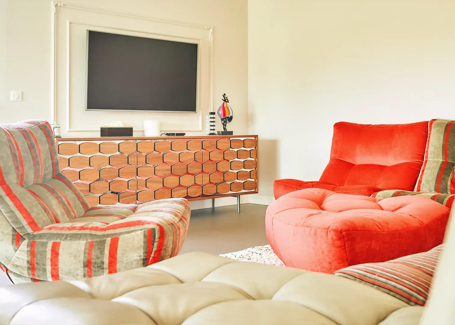 Salon design avec fauteuil rouge corail, enfilade nid d'abeille et téléviseur, photographie immobilière haut de gamme
