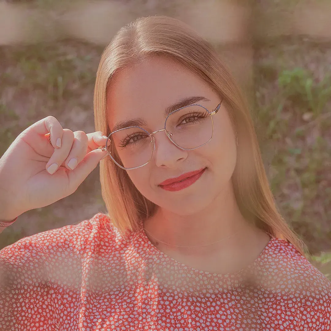 Portrait naturel en extérieur d’une jeune femme blonde ajustant ses lunettes, blouse fleurie, lumière dorée