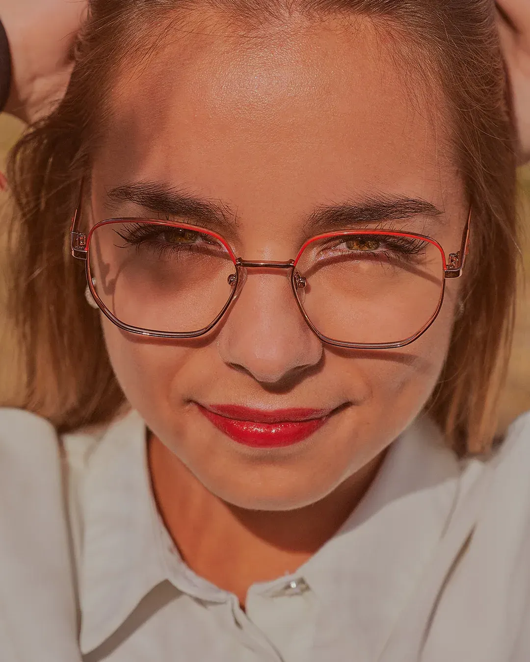 Portrait rapproché d’une femme à lunettes fines et rouge à lèvres, lumière naturelle chaude, par un photographe portraitiste