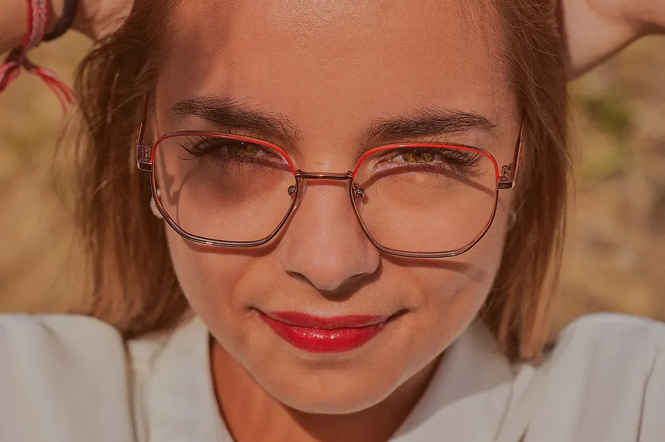 Portrait serré en lumière naturelle : jeune femme à lunettes rouges et rouge à lèvres carmin, sourire complice
