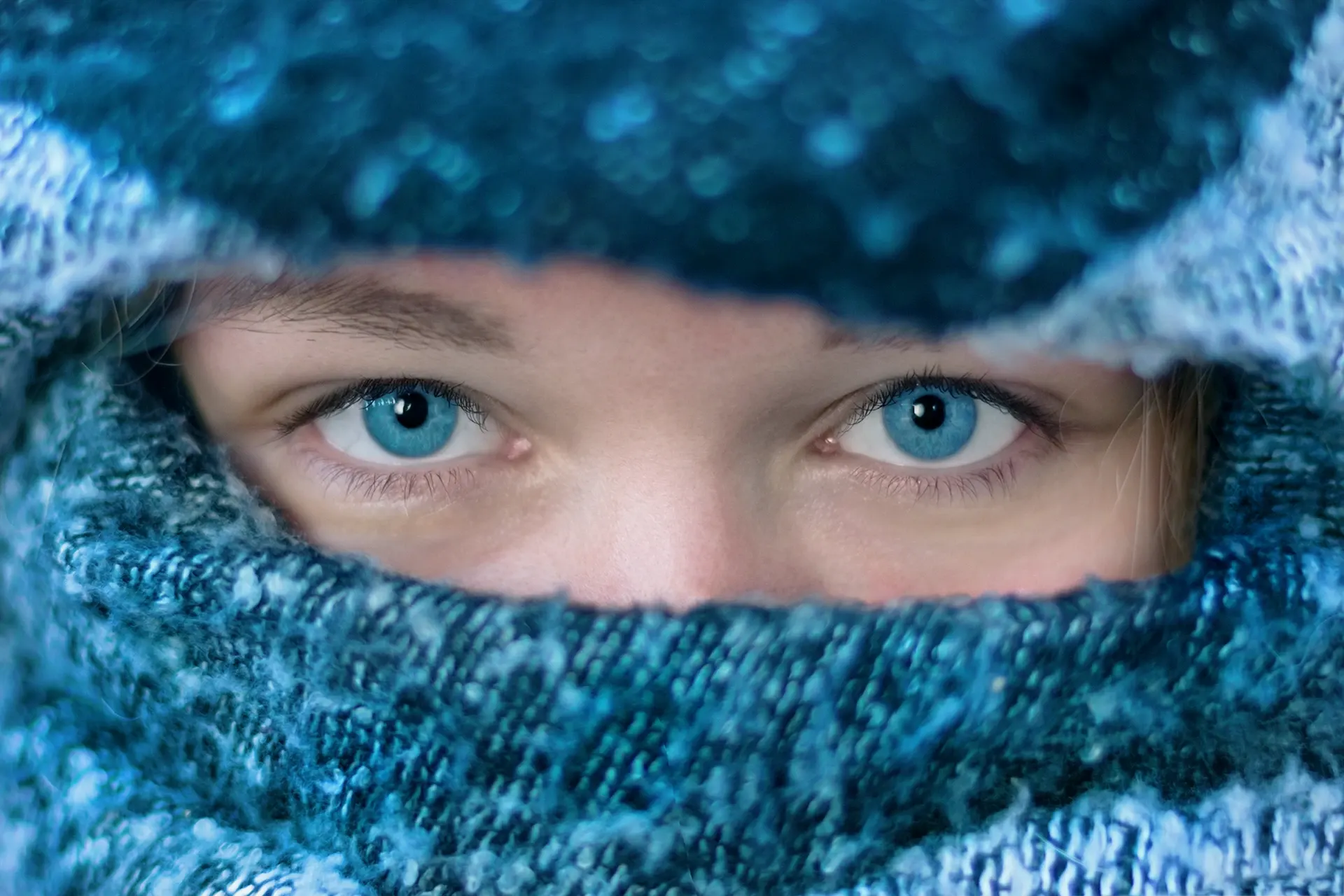 Portrait serré d’un regard bleu émergeant d’une écharpe en laine bleue, gros plan photographique studio