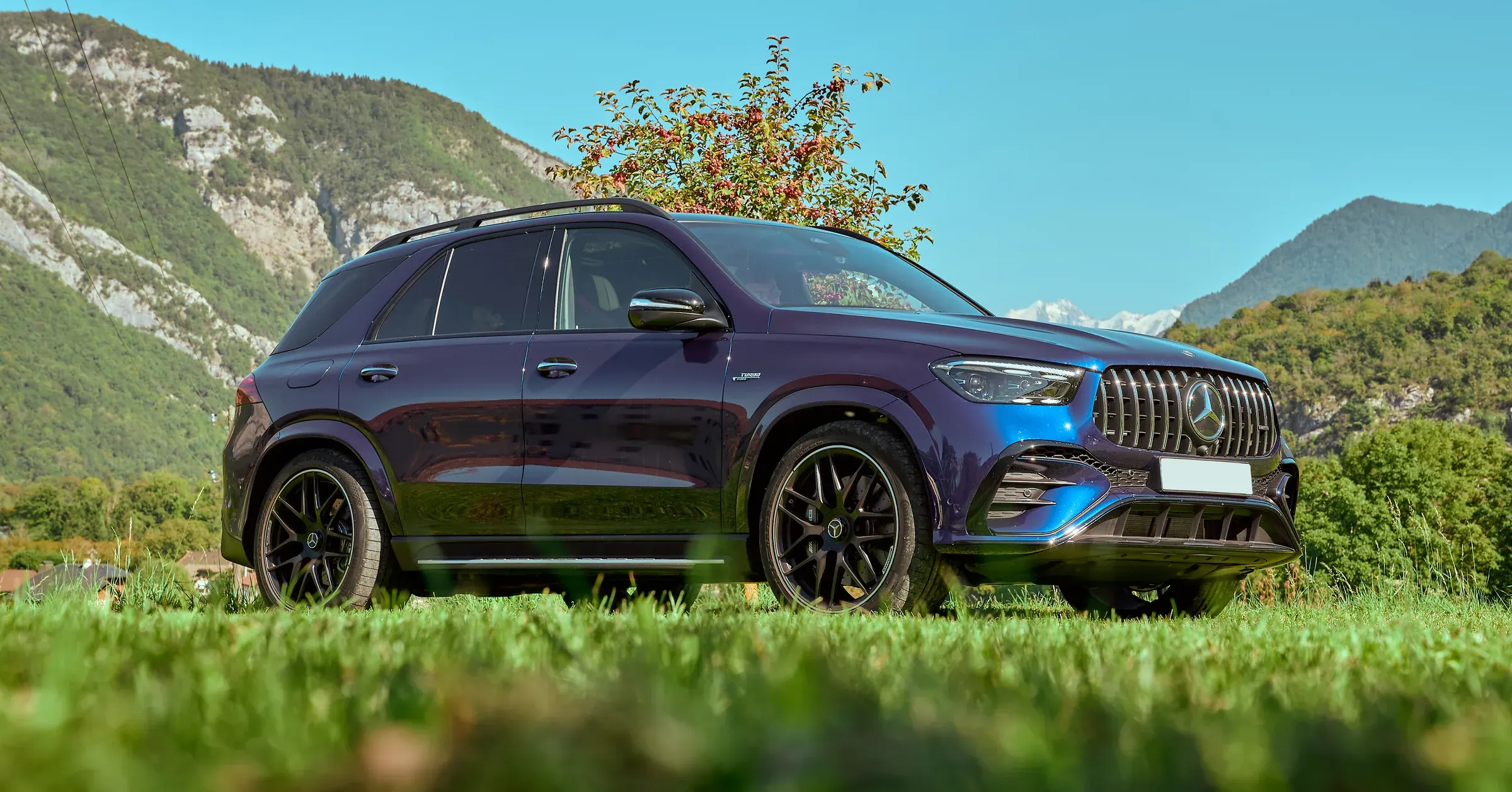 SUV Mercedes-Benz GLE AMG bleu nuit en contre-plongée sur l'herbe, montagnes de Giez en fond, photographie automobile