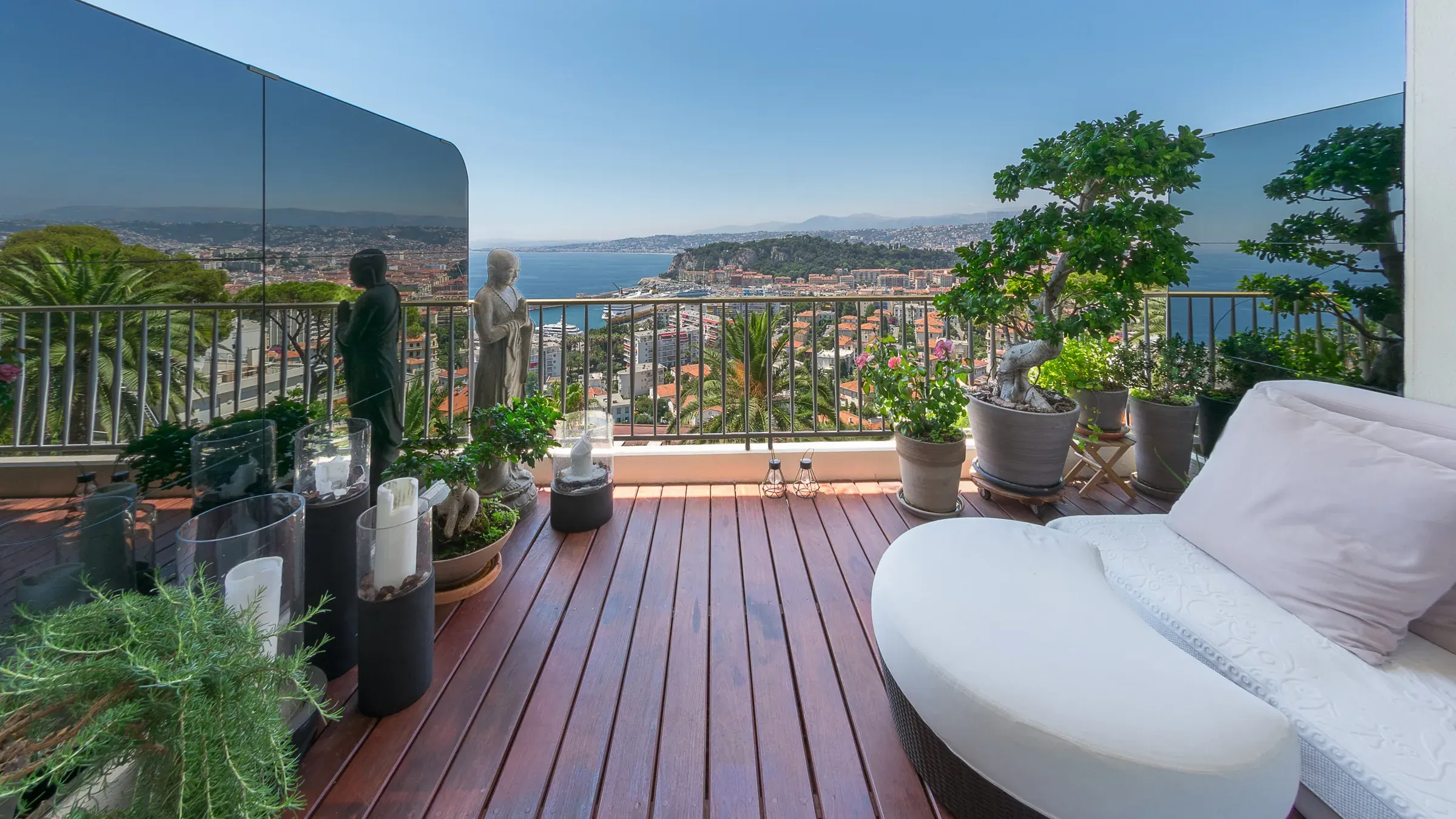 Terrasse en bois avec méridienne blanche, bonsaïs et vue panoramique sur la mer, photographe immobilier de prestige en France